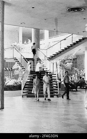Weitaufnahme mehrerer Personen in der Nähe einer offenen Treppe im Atrium des Habana Libre Hotels, Havanna, Kuba, 1964. Aus der Sammlung Deena Stryker Photographs. () Stockfoto