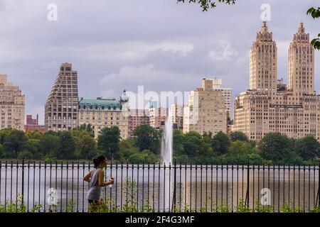 Junge Frau, die im Central Park von der Jacqueline Kennedy läuft Onassis Reservoir und mit Blick auf das Eldorado in Der Hintergrund Stockfoto