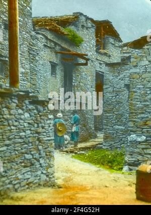 Zwei Personen, von hinten, stehen auf einem schmalen Feldweg, der sich durch die Steinmauern einer traditionellen tibetischen Stadt schlängelt, wahrscheinlich Xisuo Village, Sichuan, China, 1917. Aus der Sammlung Sidney D. Gamble Photographs. () Stockfoto