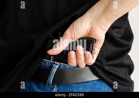 Verdeckte Pistole unter dem Jeansgürtel. Ein Mann in Jeans und einem T-Shirt hält eine Pistole in der Hand von hinten Stockfoto