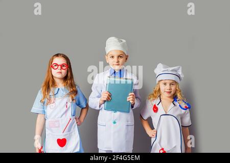 Nette kleine Kinder, die als Ärzte auf grau gekleidet sind Stockfoto