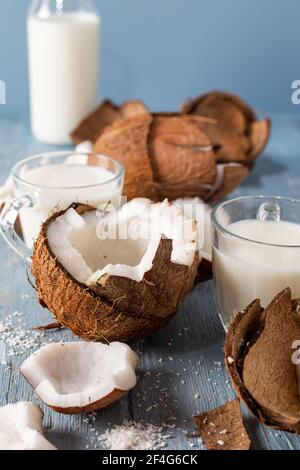 Kokosnusshälften und Stücke mit Glas Kokosmilch auf blauem Naturholzhintergrund. Stockfoto