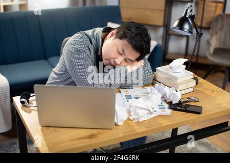 Top-Winkel-Ansicht der jungen erschöpft asiatischen Geschäftsmann schlafen auf dem Tisch nach langen Papierkram. Müde Mann in Freizeitkleidung Pause bei der Arbeit. Überarbeiteter Begriff. Online von zu Hause aus arbeiten Stockfoto