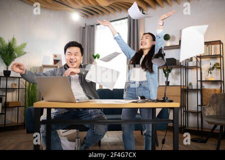 Fröhliche asiatische Büroangestellte werfen Papiere herum nach erfolgreichem Geschäftstreffen. Glücklicher Mann und Frau zufrieden mit Coworking. Business People-Konzept. Stockfoto