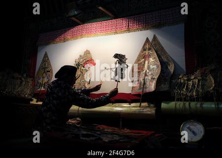 Marionettenmeister (Dalang) führt die Wayang-Kumit-Performance 'The Death of Kumbakarna' im Sonobudoyo Museum in Yogyakarta, Zentral-Java, Indonesien, auf. Auf dem Bildschirm links ist die Puppe Kumbhakarna zu sehen, während auf beiden Seiten der Leinwand die allegorischen Figuren der Gunungan zu sehen sind, die sowohl den javanischen Lebensbaum als auch den Kosmischen Berg (Berg Meru) darstellen. Das traditionelle Puppenschattentheater Wayang kulit ist auf den Inseln Java und Bali in Indonesien weit verbreitet. Jede Wayang kulit Aufführung dauert etwa acht Stunden durch die Nacht ohne Pausen und nur eine Stockfoto