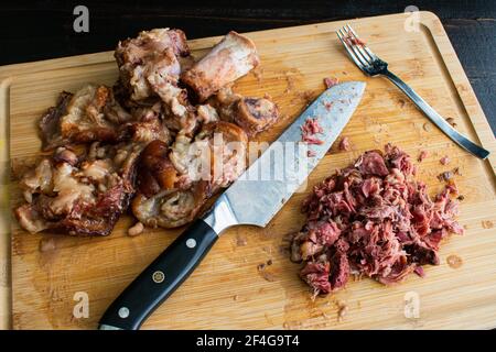 Schneiden von Fleisch aus geräuchertem Schinken Hocks: Gehacktes Fleisch mit der ausrangierten Haut und Knochen auf einem Bambus Schneidebrett Stockfoto