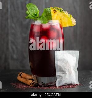 Eisgekühlter Zobo-Tee in einem hohen Glas, auf einem Schieferhintergrund, umgeben von den Zutaten des Getränks Stockfoto