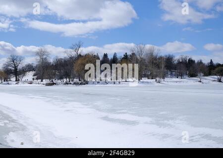 Gefrorener, schneebedeckter Kanal/See und Rücken von schneebedeckten Bäumen dahinter und ein schöner blauer, flauschiger Wolkenhimmel. Ein perfekter Wintertag in Ottawa, Ontario. Stockfoto