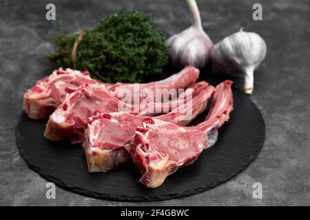 Rohe Lammkoteletts mit Knoblauch, Kräuter auf schwarzer Keramikplatte über weißem Steintisch. Draufsicht. Mit Kopierbereich. Stockfoto