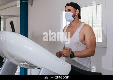 Mann, der auf einem Laufband läuft und eine Maske trägt. Covid19. Gesundheits- und Sicherheitskonzept. Stockfoto