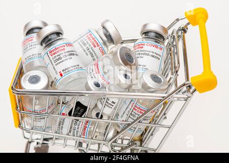 Original COVID-19 Impfampulle der Firma Moderne und Pfizer-BioNTech symbolisch in Einem Einkaufswagen mit deutschfarbener Banderole Stockfoto