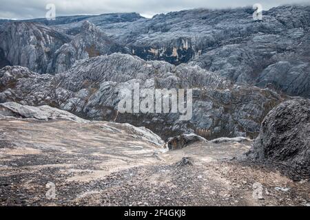 Männlicher Kletterer, der während des Aufstiegs der Carstensz Pyramid in Papua, Indonesien, der Seven Summits vom Basislager aus schwierige Felsabschnittsüberstiege aushandelt Stockfoto