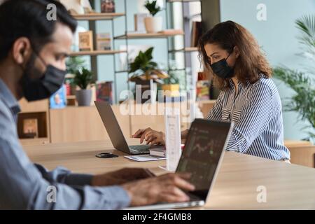 Junge lateinische Frau trägt Gesichtsmaske arbeiten auf Laptop sicheren Abstand zu halten. Stockfoto