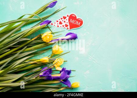 Liebe Grüße für Muttertag mit einem Strauß Narzissen, lila Iris und roten Herzen mit dem Text MAMA, Happy Mothers Day Concept.Postkarte mit Stockfoto