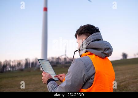 Elektroingenieur überprüft oder repariert Windenergieanlagen im Feld mit einem Tablet. Stockfoto