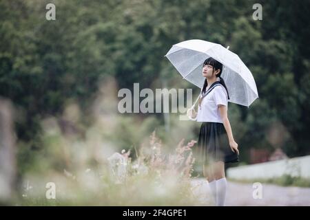 Portrait von asiatischen Schule Mädchen gehen mit Regenschirm auf die Natur Gehweg auf Regen Stockfoto