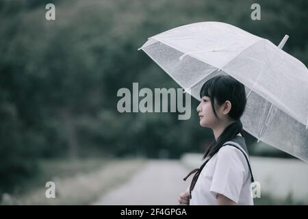 Portrait von asiatischen Schule Mädchen gehen mit Regenschirm auf die Natur Gehweg auf Regen Stockfoto