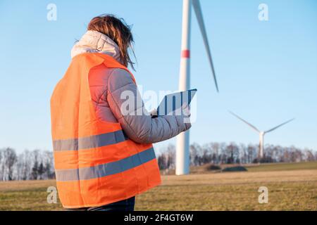 Eine Ingenieurin überprüft oder repariert Windmühlen oder Windenergieanlagen mit einem Tablet in einem orangefarbenen vesta. Stockfoto