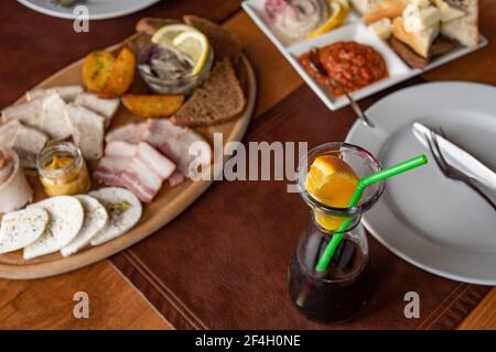 Glasflasche Glühwein mit grünem Plastiktrinkstroh und Scheibe Orangenzitrusfrucht. Tischeinstellungen von oben mit Vorspeisen auf Holz Stockfoto