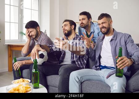 Verärgert junge Sportfans sitzen auf der Couch und beobachten schrecklich Fußballspiel im Fernsehen Stockfoto