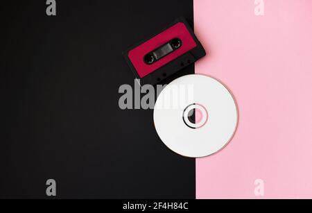 Schwarze Audiokassette und weiße Disc auf rosa-schwarzem Hintergrund. 80s. Draufsicht. Flach liegend. Stockfoto