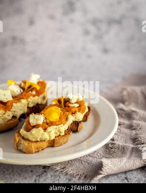 Anordnung von frisch gebackenen Kürbiskuchen-Toasts mit süßer Marmelade Und Ziegenkäse mit gelben Blütenblättern verziert und serviert Auf Platte Stockfoto