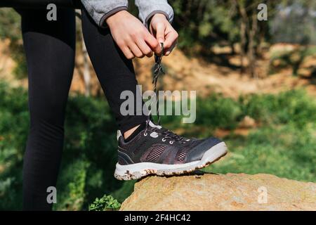 Seitenansicht der Ernte unkenntlich weibliche Wanderer binden Schnürsenkel auf Sneakers während der Pause im Sommer Abenteuer im Wald Stockfoto