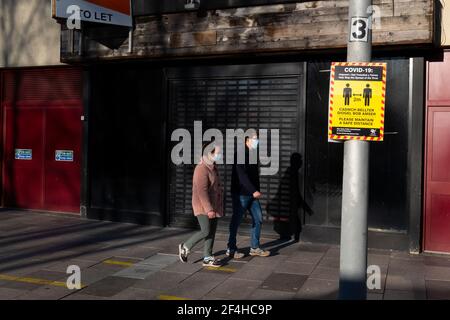Zwei Personen mit Gesichtsmasken gehen während der Sperrzeit des Coronavirus in Cardiff, Wales, Großbritannien, an einem geschlossenen Einzelhandelsgeschäft vorbei. Stockfoto