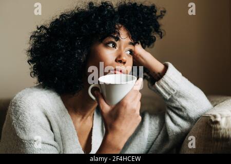 Positive afroamerikanische Frau in stilvoller Kleidung, die Telefongespräche mit dem Handy führt, während sie auf der Straße in der Nähe des Gebäudes in der Stadt läuft Stockfoto