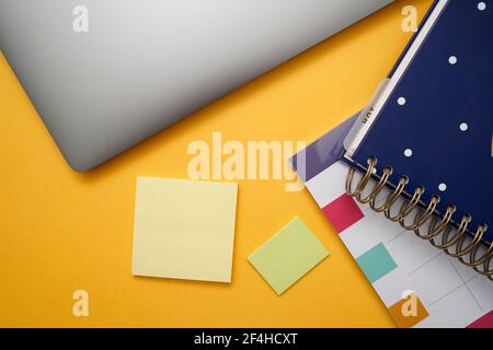 Draufsicht auf buntes Notizbuch und Planer in der Nähe von Sticky platziert Notizen und Laptop auf gelbem Tisch Stockfoto
