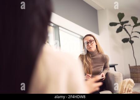 Weibliche Beraterin sitzt im Sessel und gibt Ratschläge zu unkenntlich Klient während der Psychotherapie-Termin Stockfoto