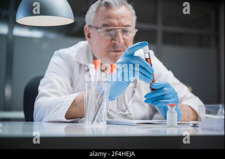 Büro des Forschers der antiviralen Medikamente. Ein älterer Apotheker hält ein Reagenzglas mit einem medizinischen Präparat in den Händen Stockfoto