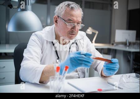 Ein medizinischer Laborant untersucht die Eigenschaften des erzeugten Impfstoffs. Er hält eine Flasche mit einer Blutprobe, die einen Impfstoff gegen die enthält Stockfoto