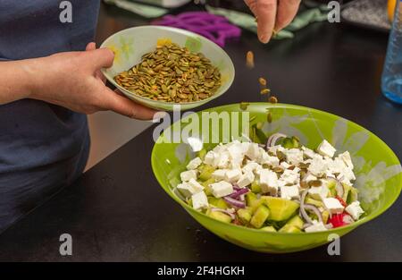 Nahaufnahme der weiblichen Zugabe von Kürbiskernen in die Salatschüssel. Gesunde Ernährung Konzept. Stockfoto