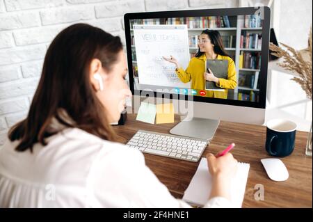 Online-Bildung per Videokonferenz. Intelligentes Mädchen, Fernstudium, Notizen machen, auf dem Computerbildschirm führt die Lehrerin eine Online-Lektion durch, die Informationen auf einem Flipchart zeigt, von zu Hause aus studiert Stockfoto