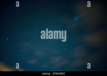 Himmel voller funkelnder Sterne und eines blau leuchtenden Planeten Auf der rechten Seite in einer bewölkten Nacht Stockfoto