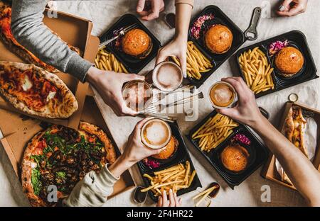 Die Leute klirren Gläser mit Bier und essen Burger und Pizza Stockfoto