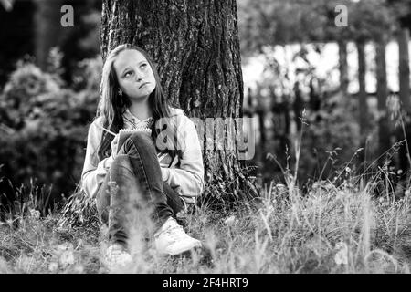 Teengirl schreibt in einem Milchbuch im Park. Schwarzweiß-Foto. Stockfoto