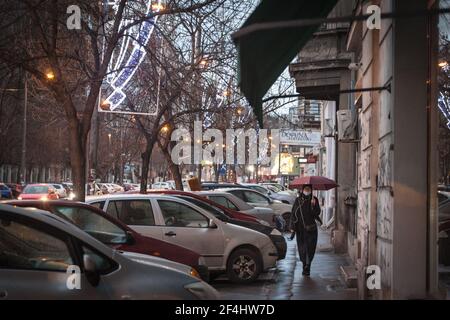 BELGRAD, SERBIEN - 27. DEZEMBER 2020: Frau mit einer Atemmaske, die während des Regenschirms in einer Straße von Belgrad unter starkem Regen läuft Stockfoto