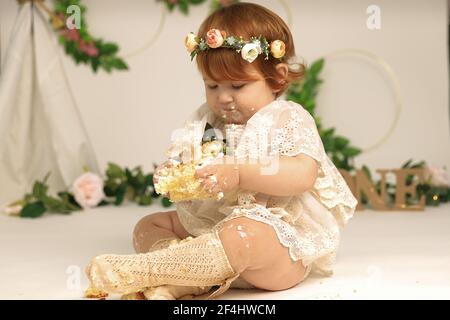 Kleines Mädchen zerschlägt einen Kuchen an seinem ersten Geburtstag. Smash Kuchen, stilisierte Foto-Session für eine Kinderparty Stockfoto