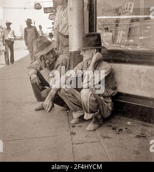 Dürrebauern säumen die schattige Seite der Hauptstraße der Stadt, während ihre Ernten auf den Feldern brennen. "Die Waschung kann uns ein wenig halten, denke ich." Sallisaw, Oklahoma. August 1936. Foto von Dorothea lange. Stockfoto