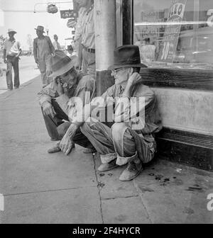 Dürrebauern säumen die schattige Seite der Hauptstraße der Stadt, während ihre Ernten auf den Feldern brennen. "Die Waschung kann uns ein wenig halten, denke ich." Sallisaw, Oklahoma. August 1936. Foto von Dorothea lange. Stockfoto