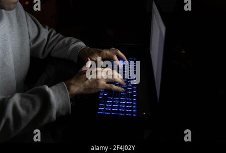 Hände des Mannes tippen auf bunten hinterleuchteten Tastatur Laptop im Dunkeln. Spät in die Nacht, lange Arbeitszeiten, Studium, anonyme Hacker-Konzepte Stockfoto