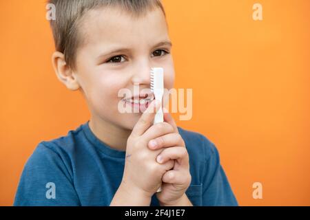 Junge ohne Milch Oberzahn in blauem T-Shirt hält Zahnbürste in der Hand auf dem orangen Hintergrund. Stockfoto