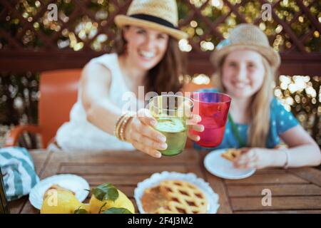 Nahaufnahme von lächelnder Mutter und Kind mit krostataklirenden Gläsern und Brunch auf der Terrasse. Stockfoto