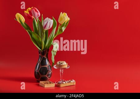 Rote Hintergrundblumen in einer Vase und drei Kuchen Stockfoto