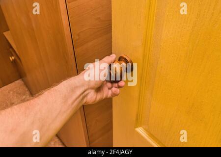 Die Hand des Typen hält den Griff und öffnet die gelbe Holztür im Innenraum des Raumes. Stockfoto