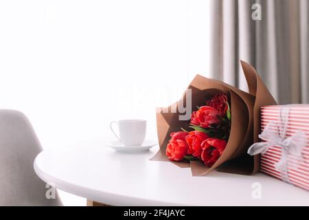 Bouquet von roten Tulpen auf dem Tisch und weiße Kaffeetasse. Konzept für Grußkarte Stockfoto