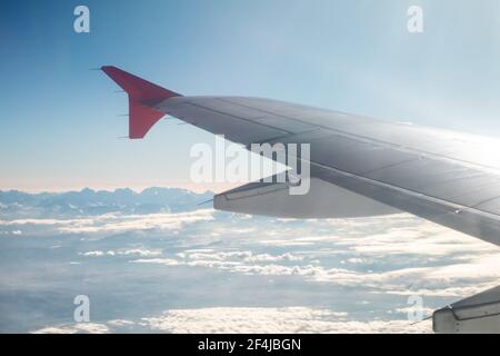 Passagierflugzeug, das über den Berggipfeln fliegt. Blick auf den Flügel Stockfoto