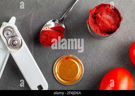 Nahaufnahme flach Lay Bild eines Löffels mit Tomatenmark in ihm. Es gibt eine bpa freie Futter Dose Tomatenpüree, ein Dosenöffner und einige reife Tomaten auf der Stockfoto